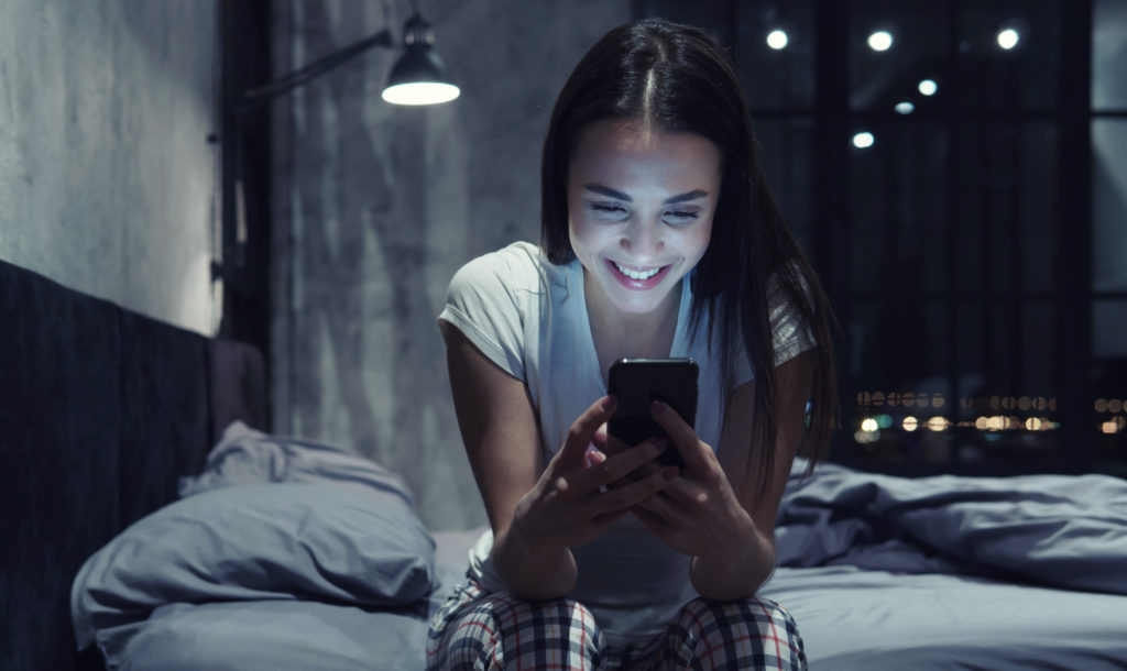 Young attractive good-looking smiling woman chatting via smartphone at night